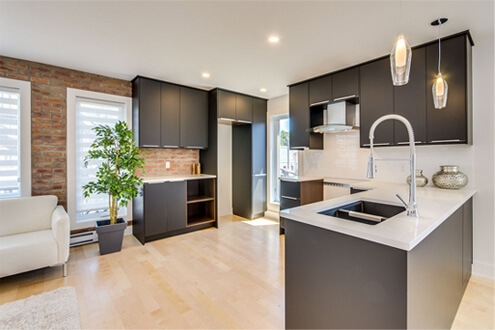 Cuisine moderne avec armoires noires, mur de brique et comptoir blanc à Montréal