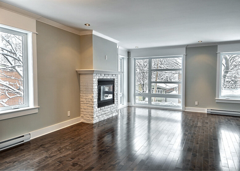 Salon rénové avec foyer mural en briques blanches et grandes fenêtres ouvrant sur l'hiver